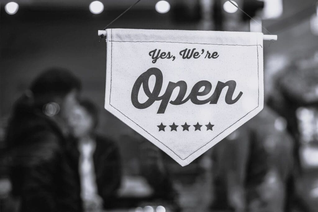 A canvas 'We Are Open' sign hanging in the window of a small business