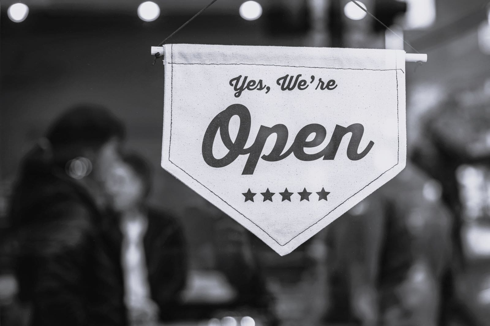 A canvas 'We Are Open' sign hanging in the window of a small business